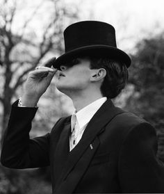 a man in a suit and top hat is holding his nose to the side as he looks off into the distance