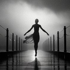 a woman is walking down a pier in the rain with her arms spread wide open