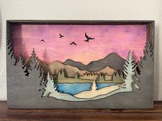 a painting on a shelf with birds flying over the water and mountains in the background