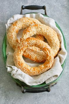 sesame bagels in a green bowl on a white cloth with a black handled handle