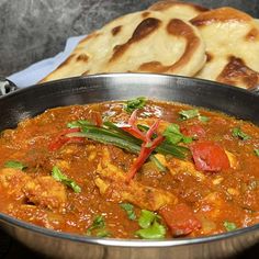 a metal bowl filled with food next to pita bread