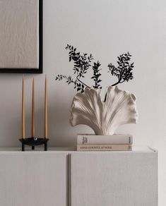 a vase with some plants on top of it next to two candles and a book