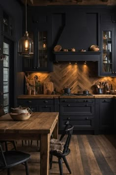 a kitchen with black cabinets and wooden floors is lit by pendant lights above the table