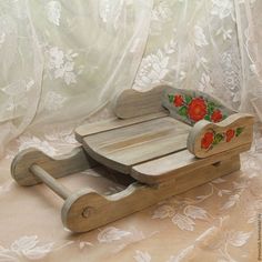 a wooden toy sled with roses painted on the front and sides, sitting on a lace covered surface