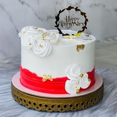 a white and red cake with gold decorations on the top is sitting on a table