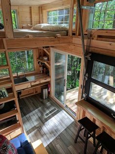 the interior of a tiny cabin with wood floors and windows, stairs leading up to an upper level kitchen area