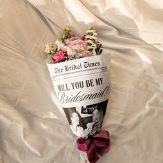 a bouquet of flowers sitting on top of a white cloth covered bed sheet with the words, will you be my bridesmaid?