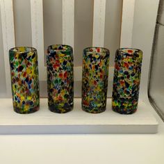 four colorful glass vases sitting on top of a white shelf next to a window