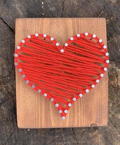 a red string heart is on a wooden board with white beads and wood planks