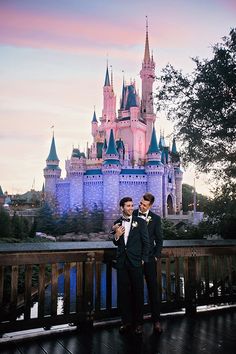 two young men standing in front of a castle at dusk with their arms around each other