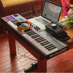 an electronic keyboard sitting on top of a wooden table next to a laptop and headphones