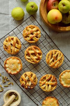 several small pies on a cooling rack next to some apples