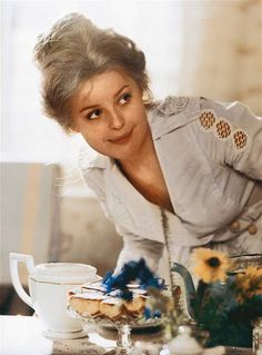 an old photo of a woman leaning over a table with food and flowers on it