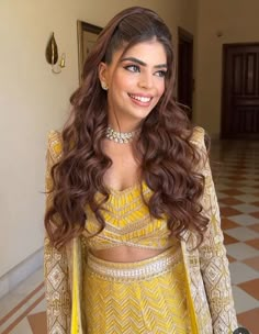 a woman with long hair wearing a yellow outfit and smiling at the camera while standing in a hallway