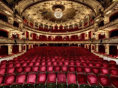 an empty theater with red seats and chandeliers on the ceiling, looking down at the stage