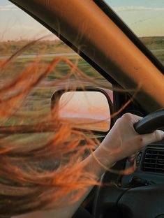 the woman is driving her car with red hair blowing in the wind