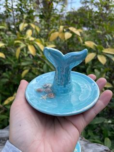 a hand holding a blue plate with a small whale tail on it's side