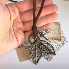 a hand holding a brown leather cord with a leaf charm on it and some letters in the background