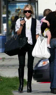 a woman walking down the street with a baby in her arms and two other people behind her