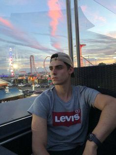 a man sitting on top of a bench next to a ferris wheel at dusk with the sky in the background