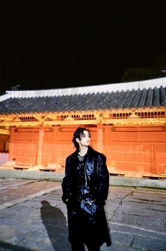 a man standing in front of a building at night with his eyes closed and one hand on his hip