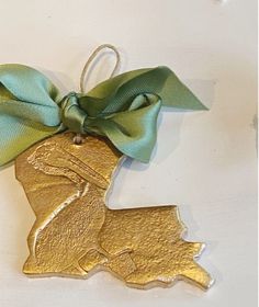 a gold ornament with a green bow hanging from it's side on a white surface