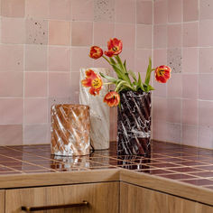 two vases with tulips in them on a counter next to a pink tiled wall