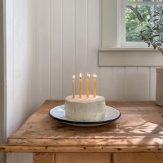 a white cake with five lit candles sitting on top of a wooden table