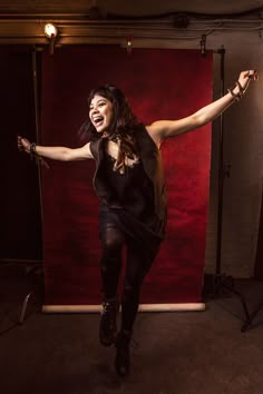 a woman in black is dancing with her arms out and legs spread wide as she smiles at the camera