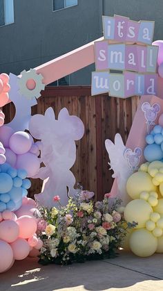 some balloons and flowers in front of a small world sign on the side of a building