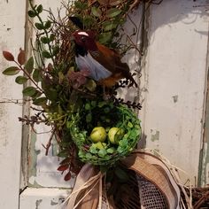 a bird sitting on top of a wreath filled with fruit and greenery next to an old door