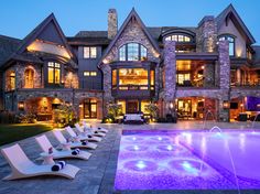 an outdoor swimming pool with chaise lounges in front of a large house at night