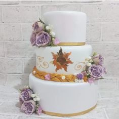 a three tiered wedding cake with purple flowers on the bottom and gold trimmings