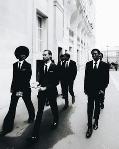 black and white photograph of men in suits walking down the street with one man wearing a hat