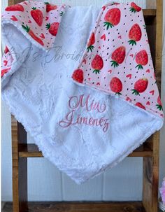 a white towel with red strawberries on it sitting on a wooden chair next to pink flowers