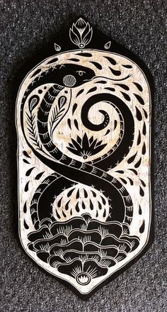 an intricately designed wooden plaque with a snake on it's side, in black and white