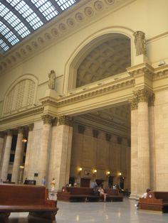 the inside of a large building with many benches and people sitting on them in it