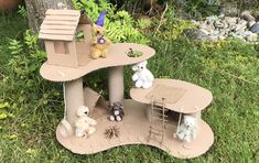 there are many stuffed animals in this miniature dollhouse house on the grass with trees and bushes behind it