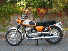 an orange and black motorcycle parked in front of a fence