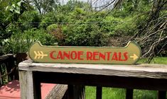 a wooden sign that says canoe rentals on the side of a deck in front of some trees