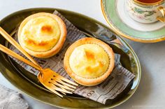 two mini quiche pies on a plate next to a tea cup and fork