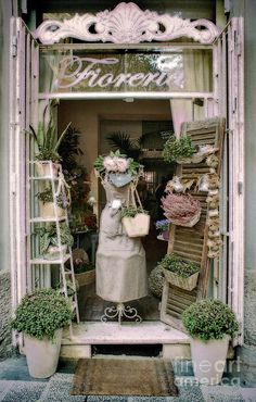 an old fashion store with flowers and plants in the front window, surrounded by potted plants