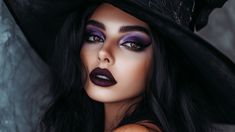 Glam Witch Makeup: A woman wearing dark, bold makeup, including deep purple lipstick and smoky, dramatic eyeshadow. She has a subtle sparkle on her cheekbones and is wearing a black witch hat with flowing hair. Halloween makeup ideas. Smoky Halloween Makeup, Witch Makeup Women, Elegant Witch Makeup, Halloween Makeup Looks Witchy, Witch Queen Makeup, Sorceress Makeup Halloween, Purple Witch Makeup Halloween