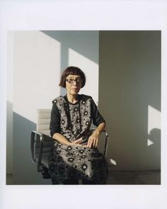 an older woman sitting in a chair with her hands on her knees and looking off to the side