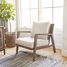 a chair sitting in front of a window next to a rug and potted plant