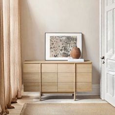 a vase sitting on top of a wooden dresser next to a window with drapes