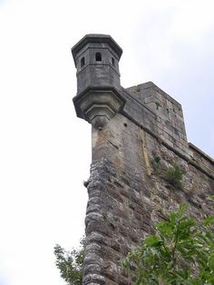 an old stone tower with a clock on it's side and trees in the foreground