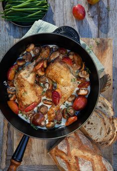 a pan filled with chicken and mushrooms on top of a wooden table next to bread