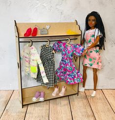 a doll is standing next to a toy wardrobe with clothes on it and shoes hanging from the door