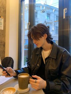 a man sitting at a table with a cup of coffee looking at his cell phone